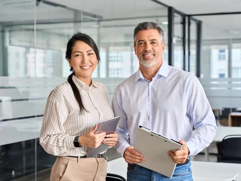 Two business partners smiling and holding tablets in a bright business directory office